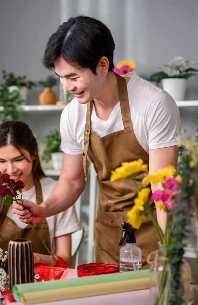Asian young florist couple completing beautiful bouquet in flower shop.